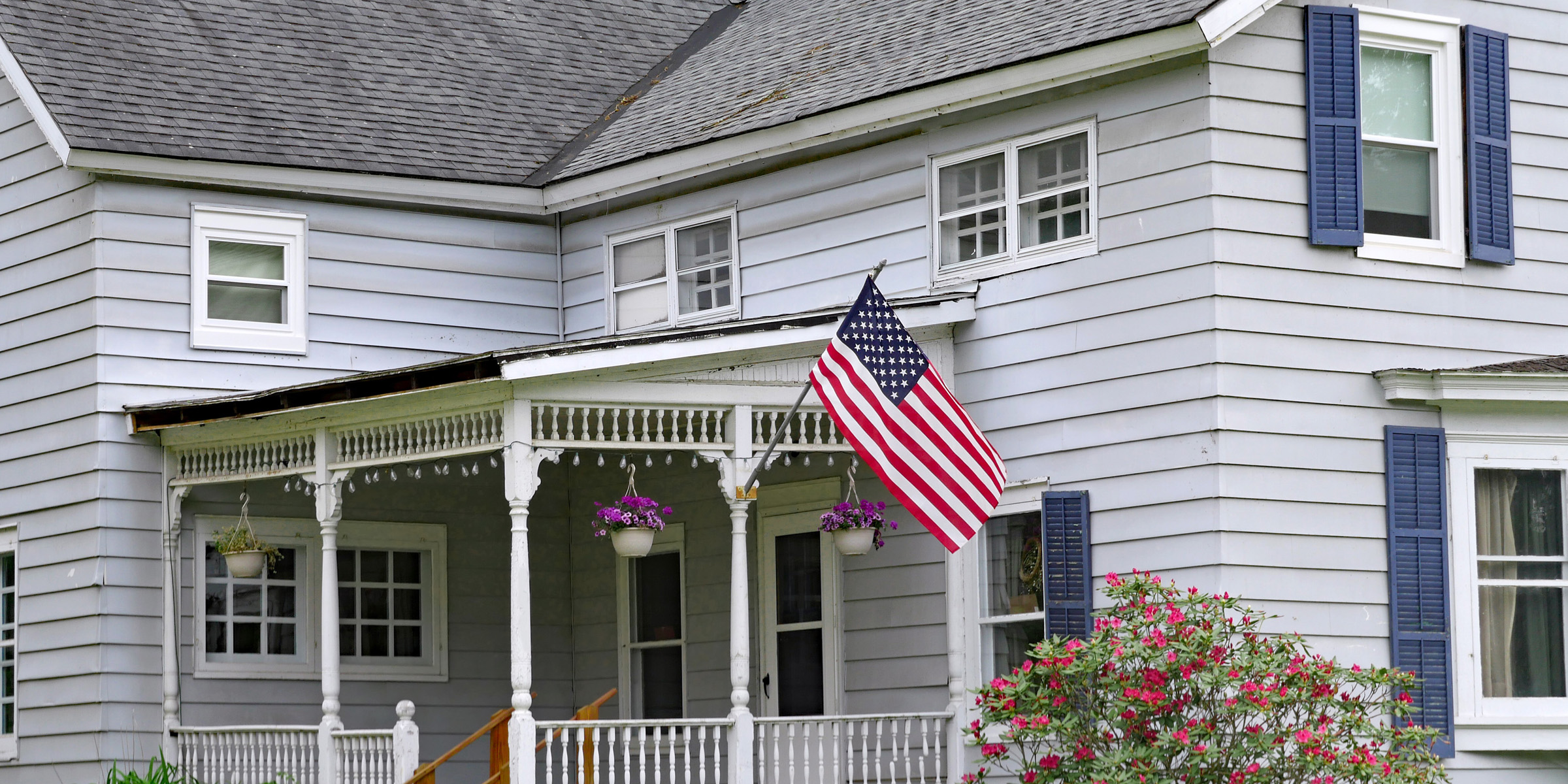 traditional style clapboard house with large porch and american flag
