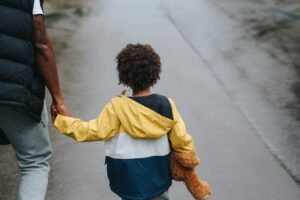 child holding teddy bear and parents hand