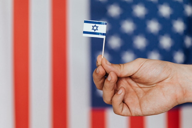 person holding small Israeli flag in front of american flag
